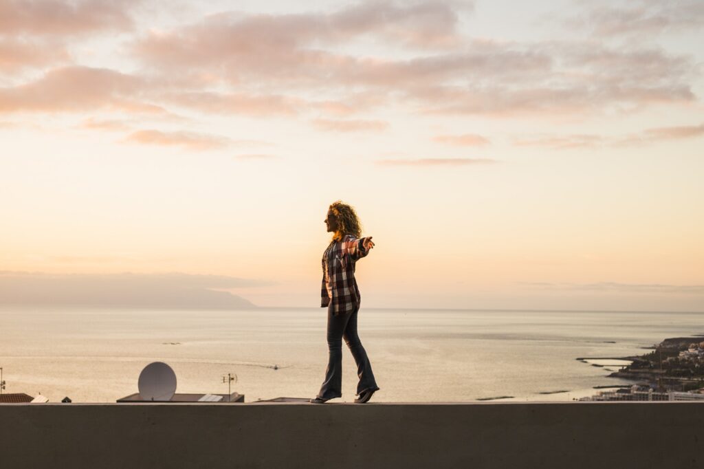 Young adult woman standing and walking free balanced with ocean coast view in background